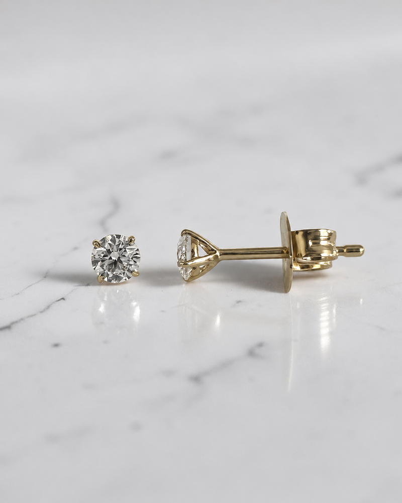 0.30ct round brilliant lab grown diamond martini stud earrings in 18ct yellow gold with E/F VS1 diamonds on a white marble background.