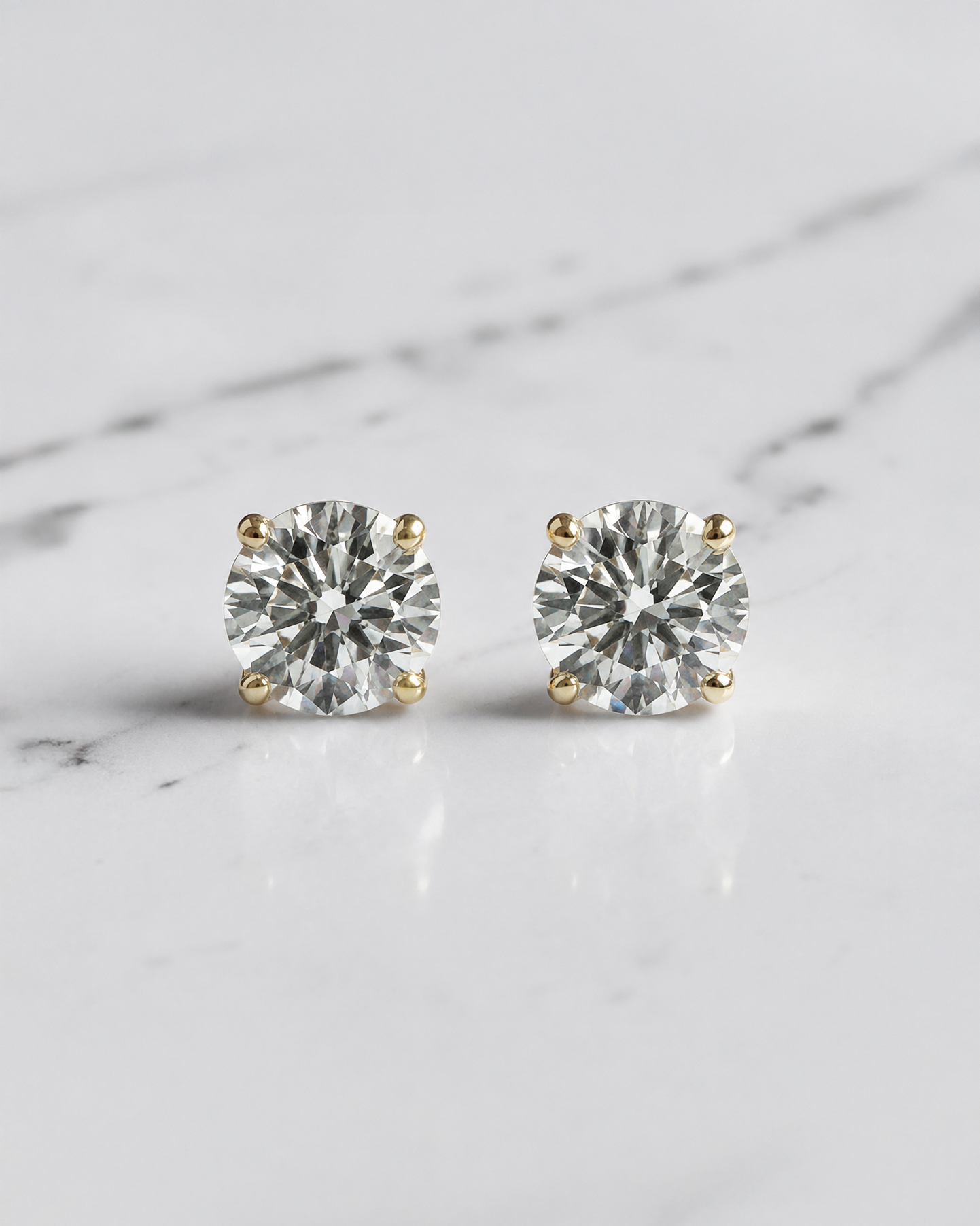 0.30ct round brilliant lab grown diamond martini stud earrings in 18ct yellow gold with E/F VS1 diamonds on a white marble background.