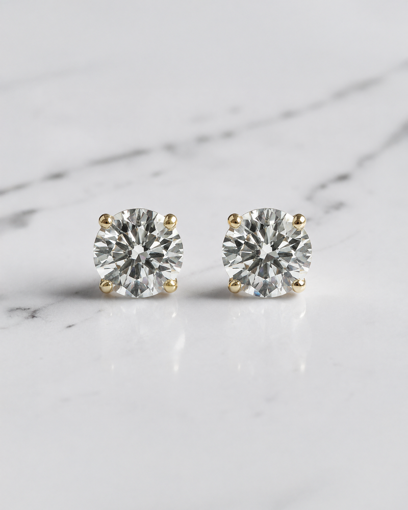 0.30ct round brilliant lab grown diamond martini stud earrings in 18ct yellow gold with E/F VS1 diamonds on a white marble background.