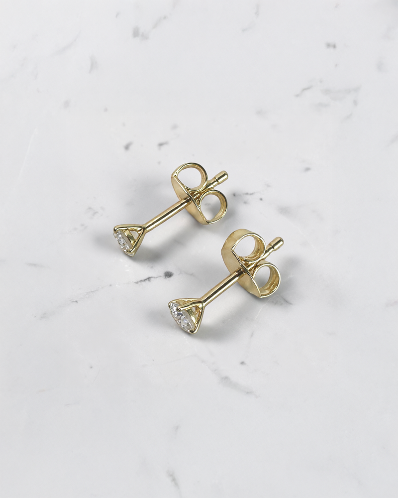 0.30ct round brilliant lab grown diamond martini stud earrings in 18ct yellow gold with E/F VS1 diamonds on a white marble background.