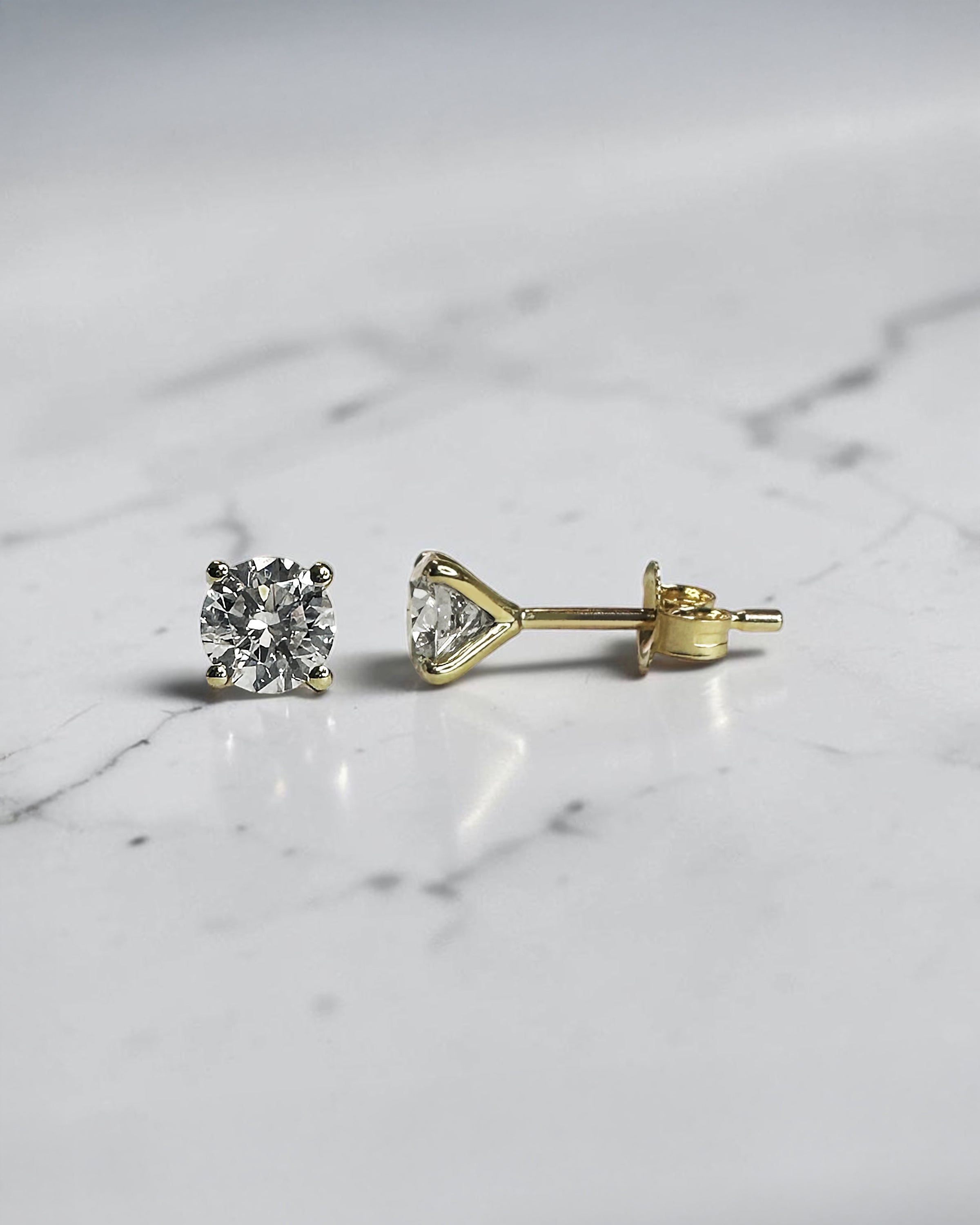 1ct round brilliant lab grown diamond stud earrings in a 4 prong martini setting with 0.50ct E/F VS1+ diamonds in yellow gold.