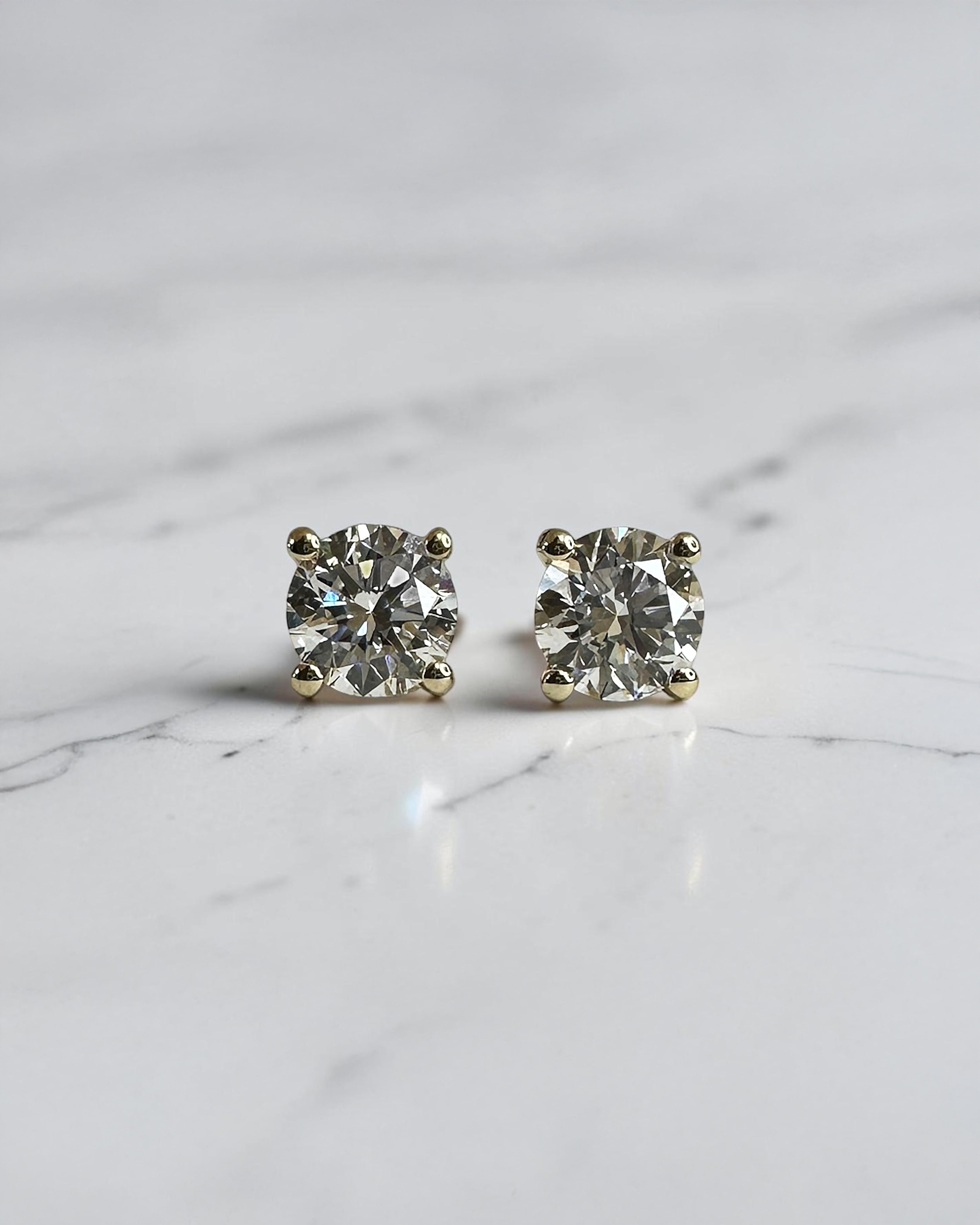 1ct round brilliant lab grown diamond stud earrings in a 4 prong martini setting with 0.50ct E/F VS1+ diamonds in yellow gold.