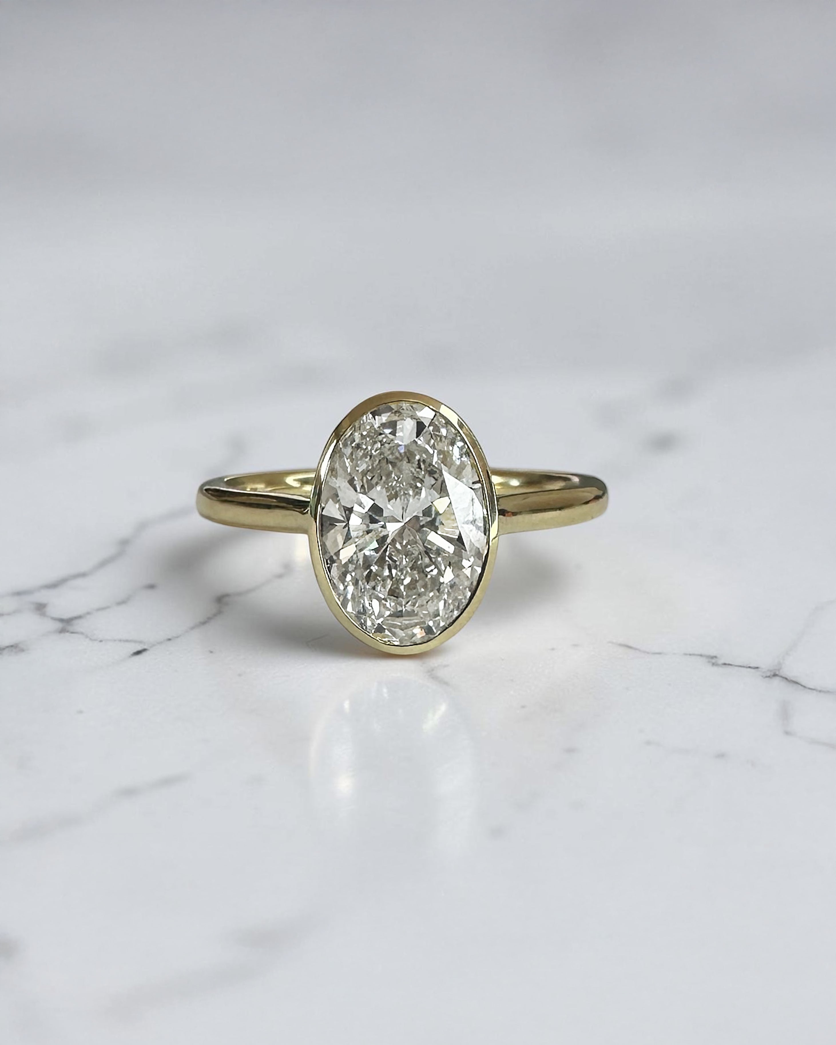 2ct oval cut lab grown diamond bezel set engagement ring in yellow gold with polished solitaire band