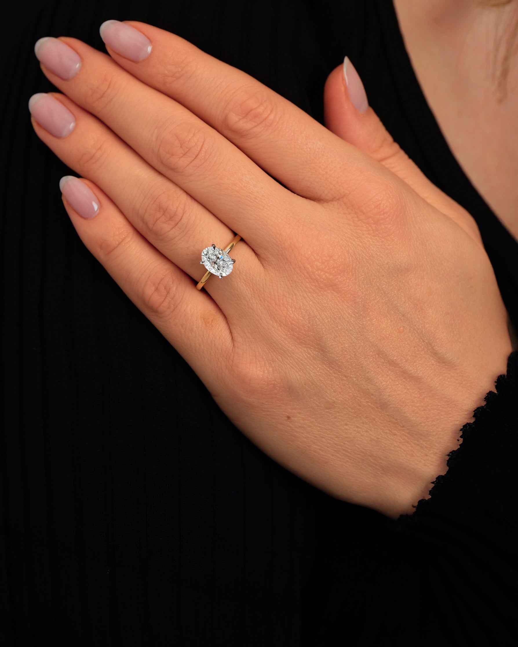 2ct lab grown oval cut diamond set in a two tone 18kt yellow gold plain band solitaire, hidden halo engagement ring on hand