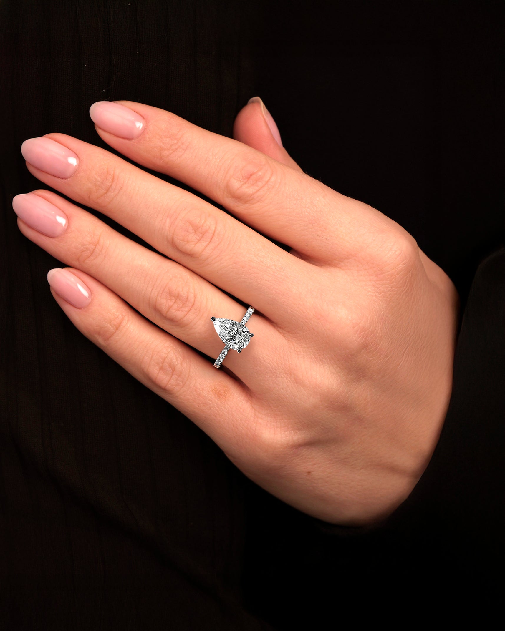 2ct pear cut lab grown diamond engagement ring on hand with tapered diamond shoulder band and lotus three prong setting in platinum, handmade in London.