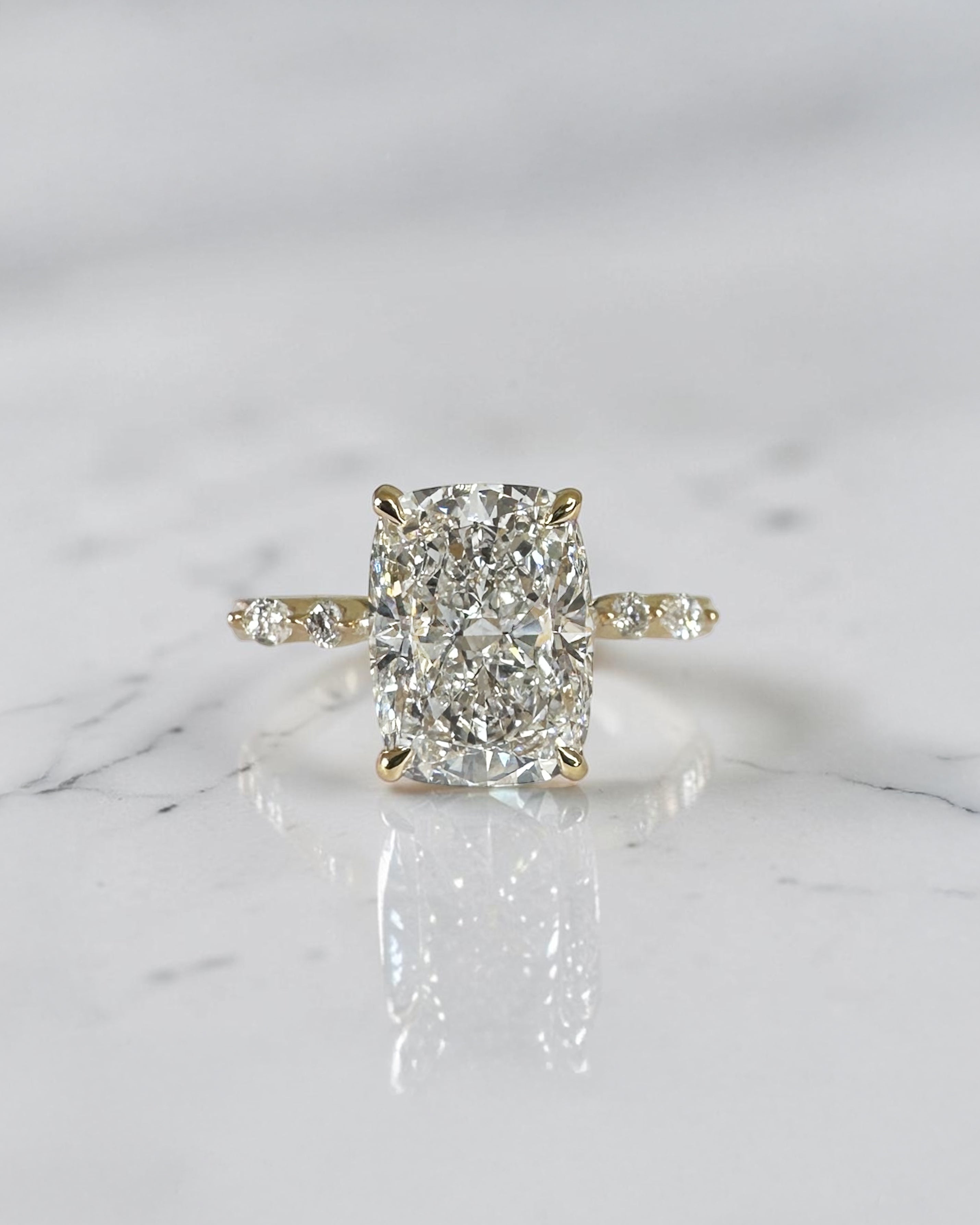 3ct elongated cushion cut lab grown diamond engagement ring featuring a hidden halo, floating head setting and marquise diamond band in 18kt yellow gold.
