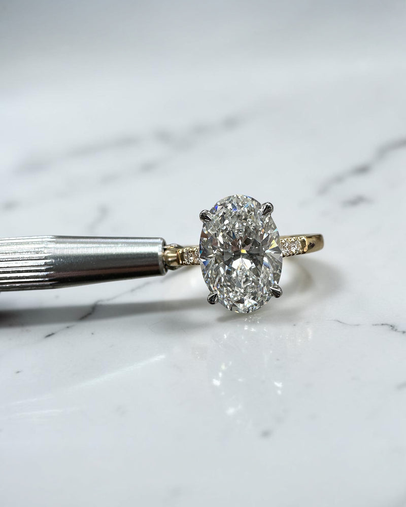 3ct oval cut lab grown diamond engagement ring with a cathedral setting, partial pavé diamond band and diamond wrap around hidden halo. Handmade in London and available in platinum or 18kt yellow gold.
