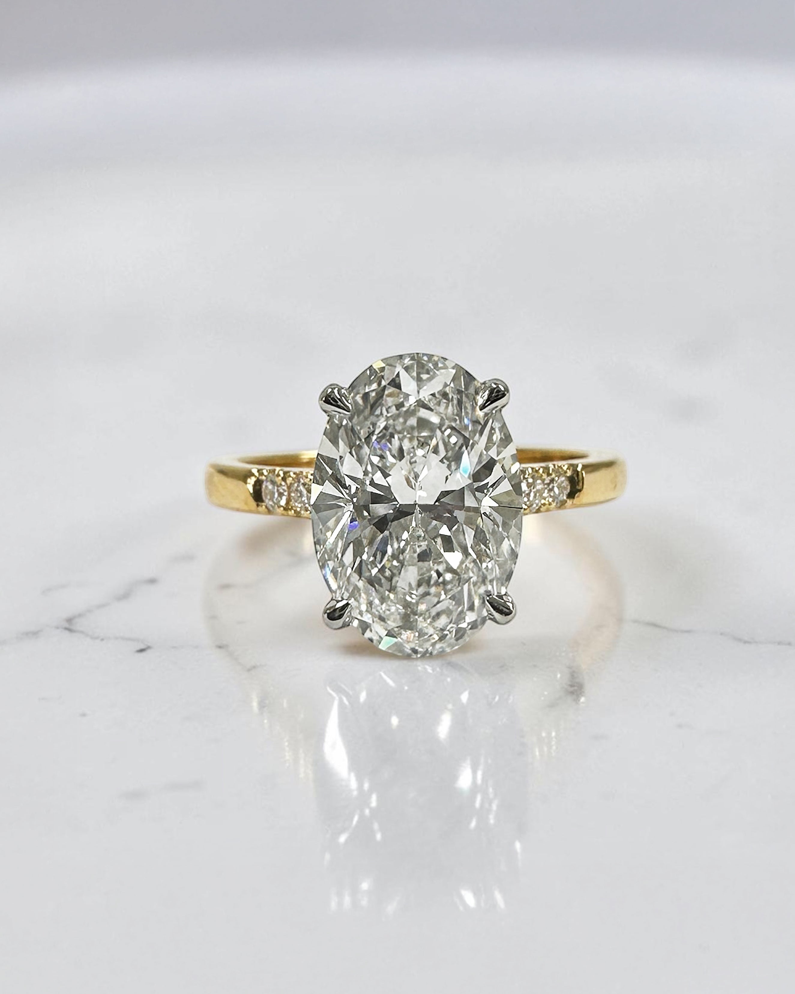 3ct oval cut lab grown diamond engagement ring with a cathedral setting, partial pavé diamond band, and diamond wrap around hidden halo. Handmade in London and available in platinum or 18kt yellow gold.