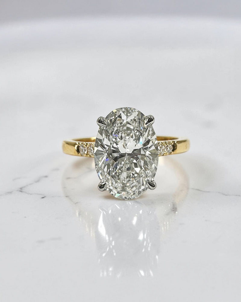 3ct oval cut lab grown diamond engagement ring with a cathedral setting, partial pavé diamond band, and diamond wrap around hidden halo. Handmade in London and available in platinum or 18kt yellow gold.
