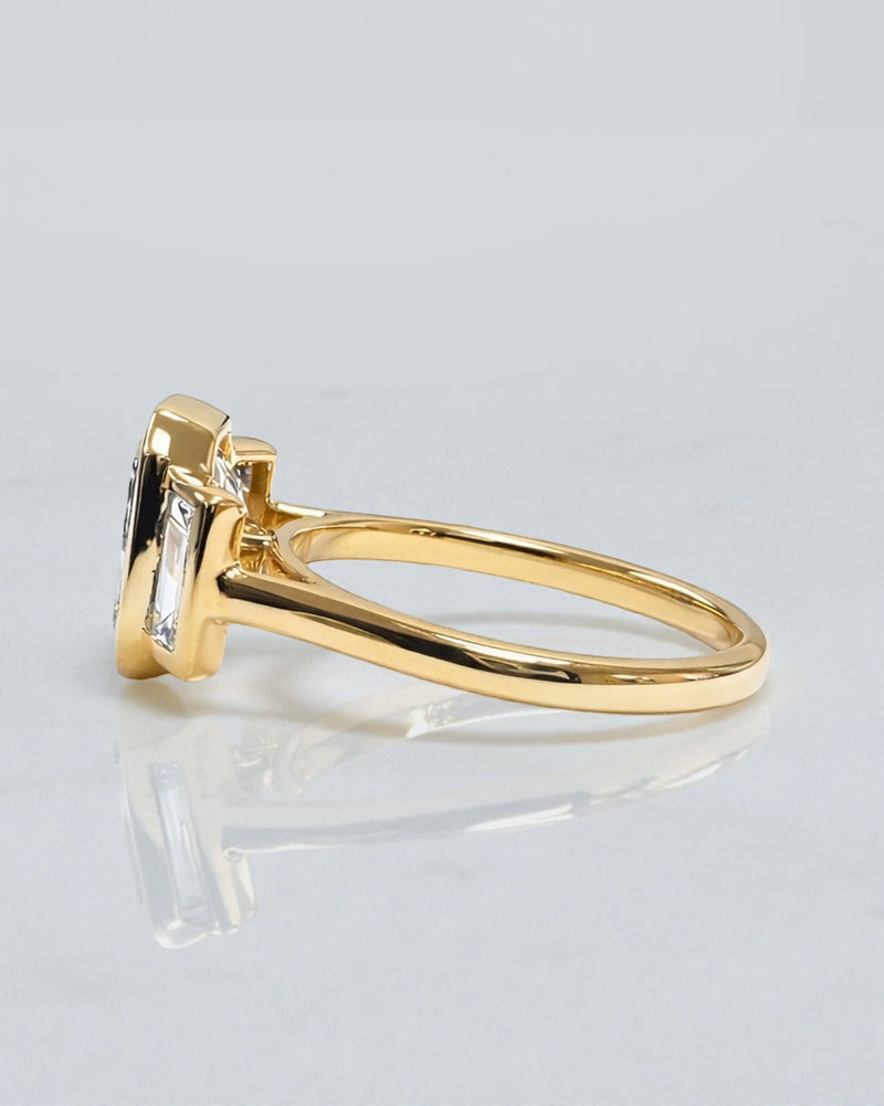 Angled view of 3ct emerald cut lab grown diamond bezel trilogy ring with baguette side diamonds in yellow gold