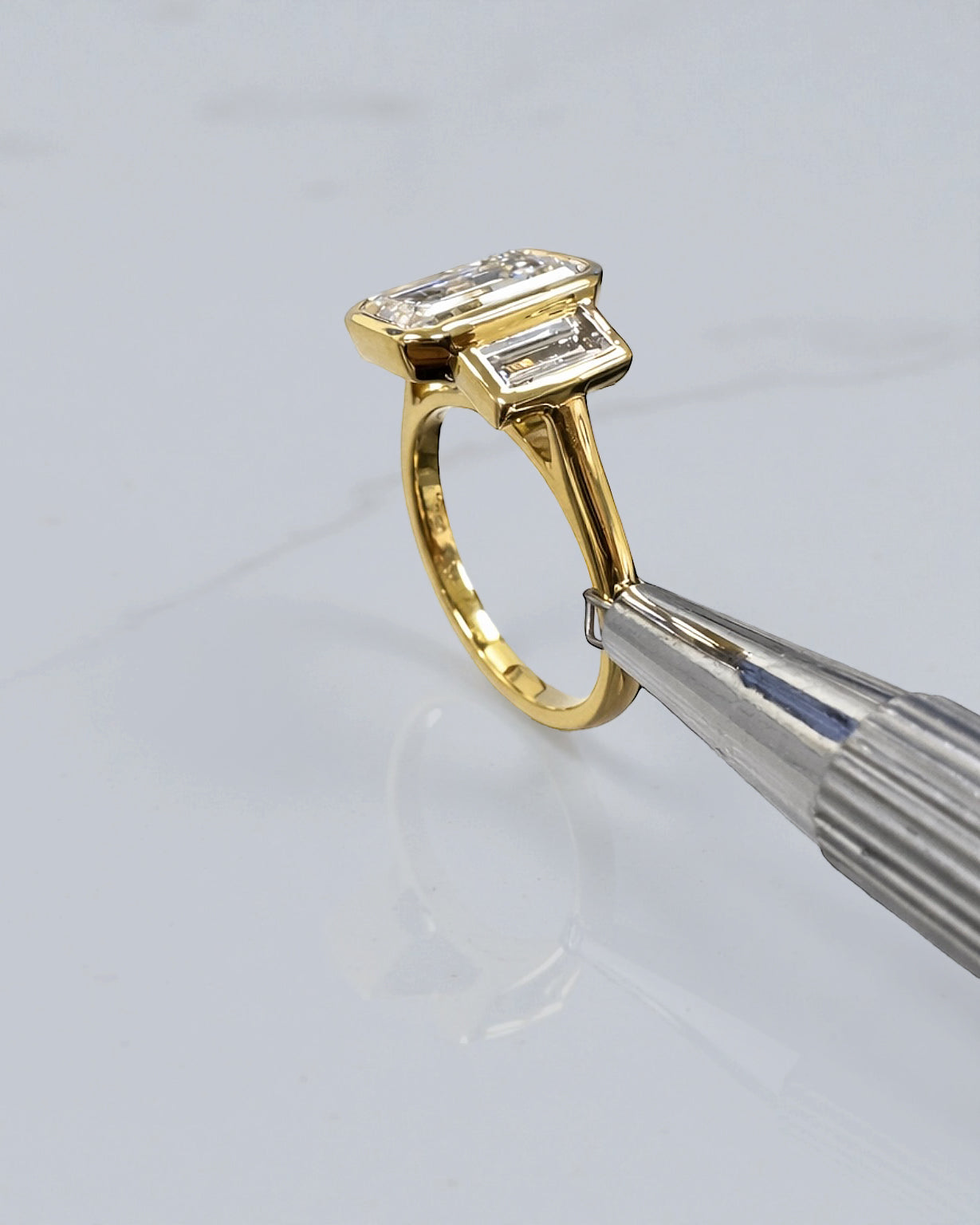 Side view of 3ct emerald cut bezel set trilogy ring with tapered baguette side stones in yellow gold