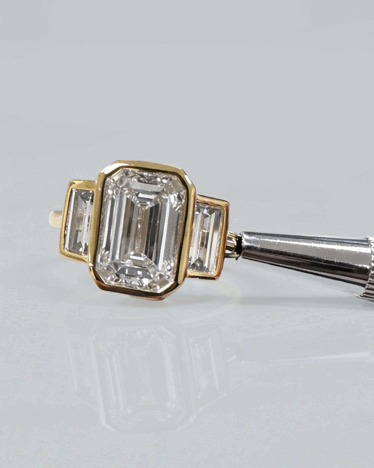 3ct emerald cut lab grown diamond bezel set trilogy engagement ring with tapered baguette side diamonds in 18kt yellow gold
