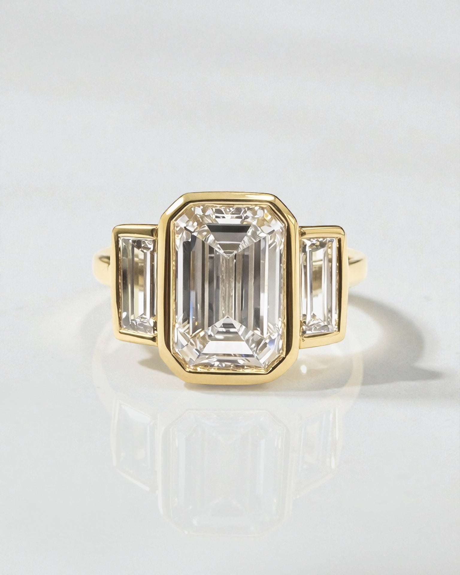 3ct emerald cut lab grown diamond bezel set trilogy engagement ring with tapered baguette side diamonds in 18kt yellow gold