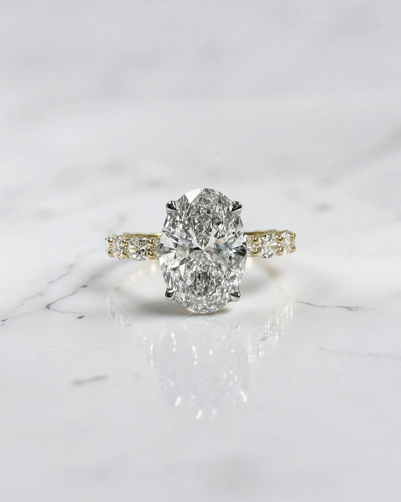 3ct oval cut lab grown diamond hidden halo engagement ring with east west oval diamond band in two tone platinum and 18kt yellow gold.