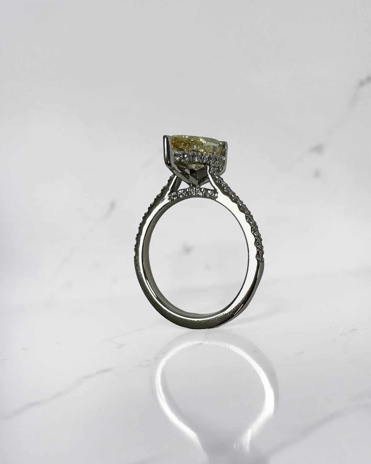 Side profile of yellow pear cut diamond engagement ring showing cathedral shoulders and diamond bridge
