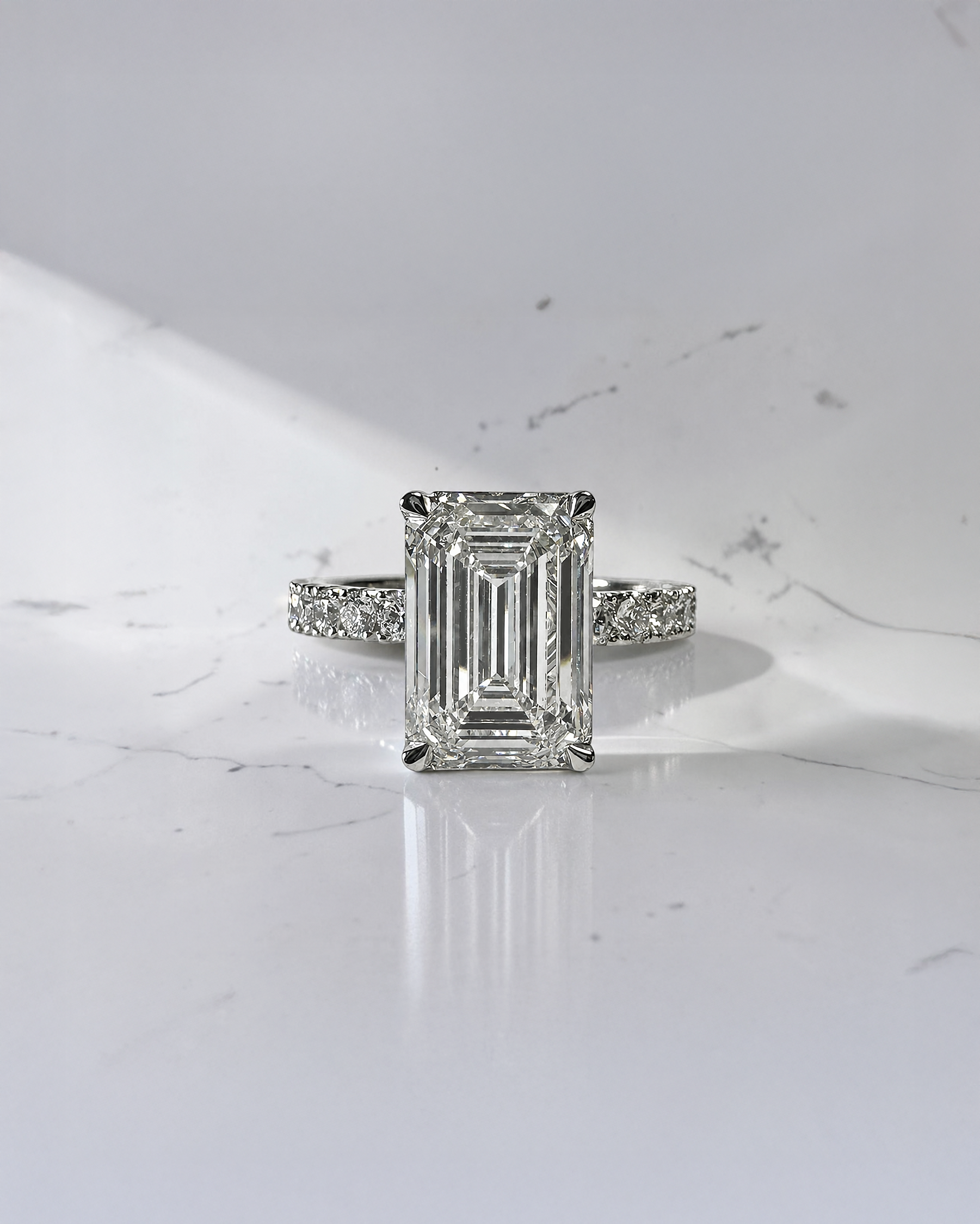 4ct emerald cut lab grown diamond engagement ring with floating diamond shoulder band and diamond wrap around hidden halo in platinum.