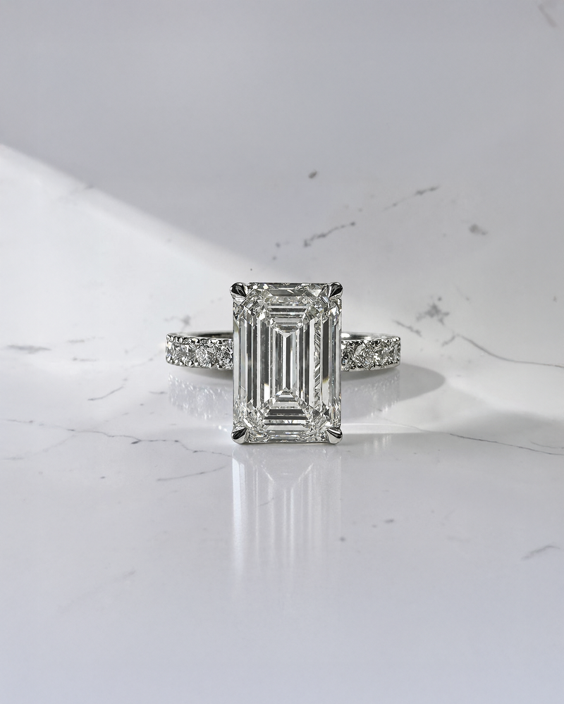 4ct emerald cut lab grown diamond engagement ring with floating diamond shoulder band and diamond wrap around hidden halo in platinum.