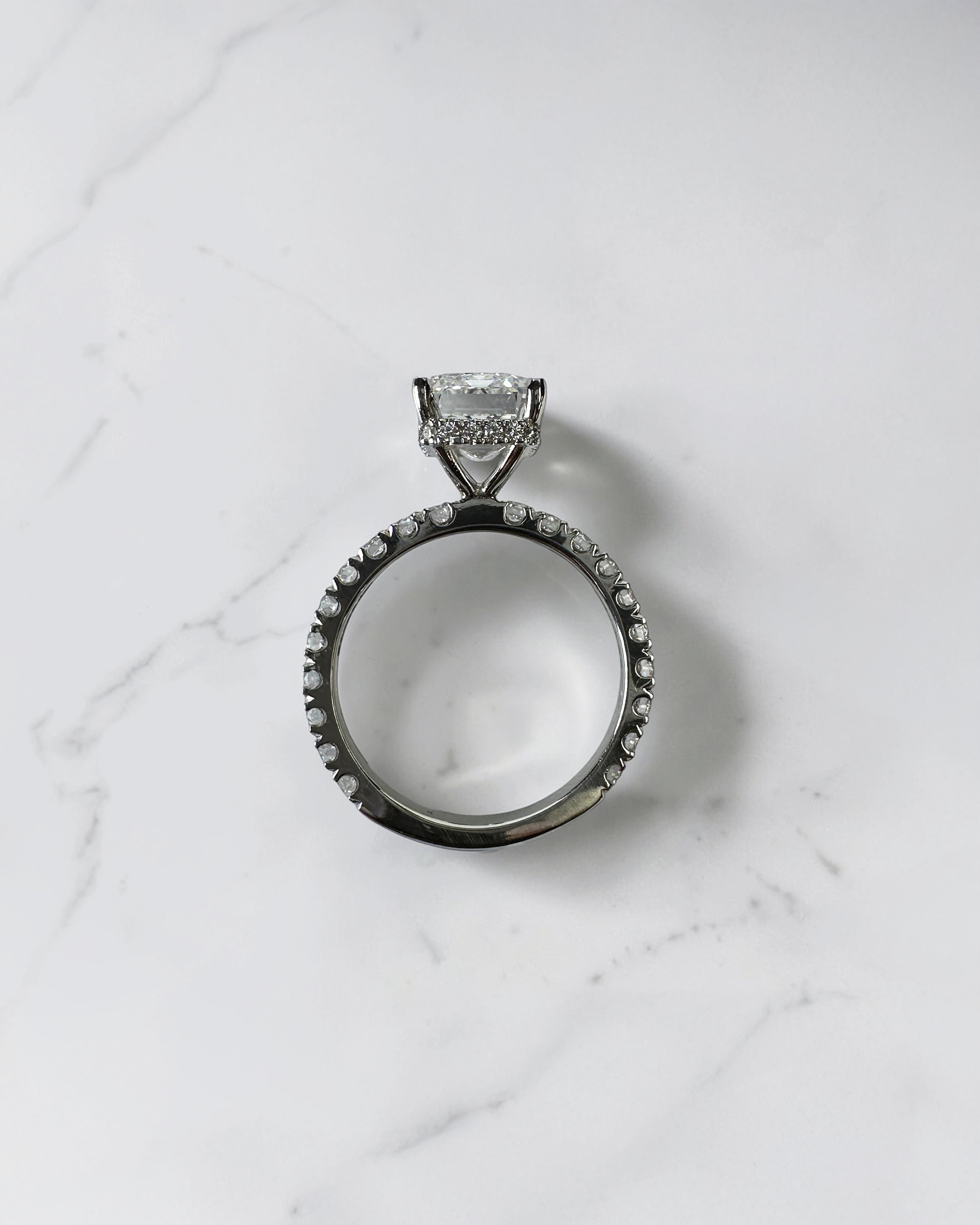 4ct emerald cut lab grown diamond engagement ring with floating diamond shoulder band and diamond wrap around hidden halo in platinum.