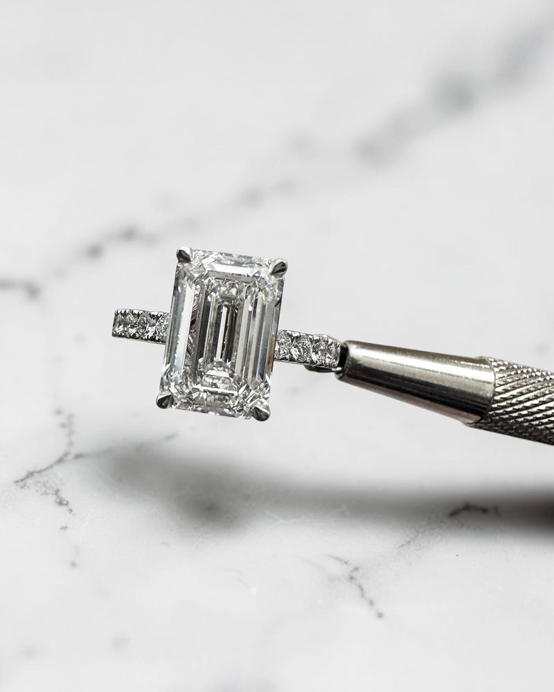 4ct emerald cut lab grown diamond engagement ring with floating diamond shoulder band and diamond wrap around hidden halo in platinum.