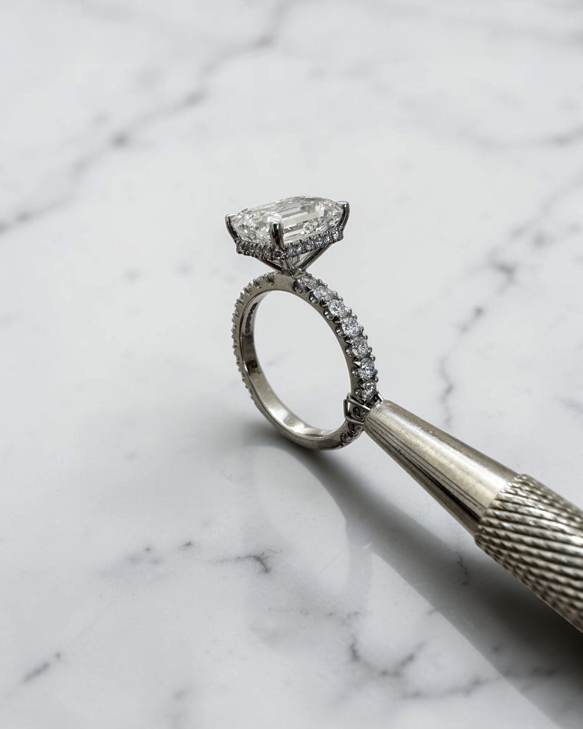4ct emerald cut lab grown diamond engagement ring with floating diamond shoulder band and diamond wrap around hidden halo in platinum.