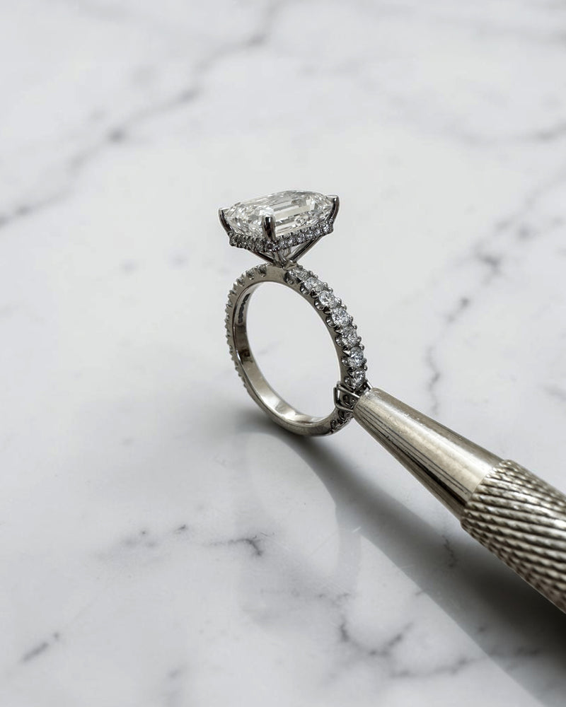 4ct emerald cut lab grown diamond engagement ring with floating diamond shoulder band and diamond wrap around hidden halo in platinum.
