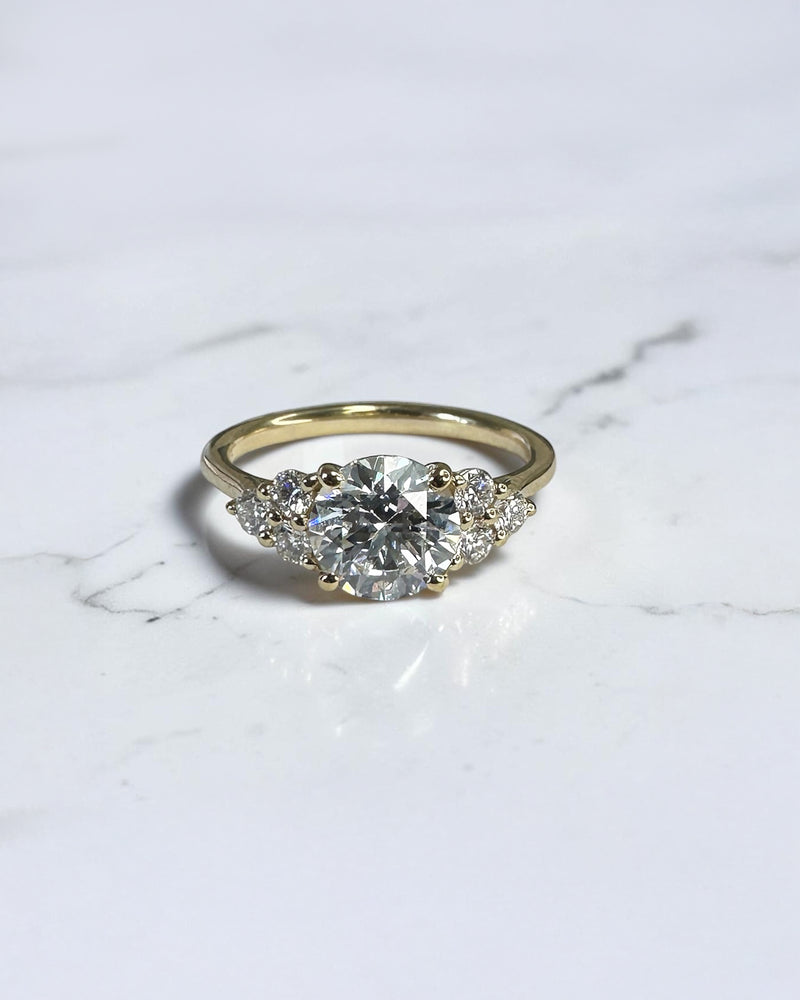 1.50ct round brilliant lab grown diamond trefoil engagement ring with diamond cluster shoulders in yellow gold.