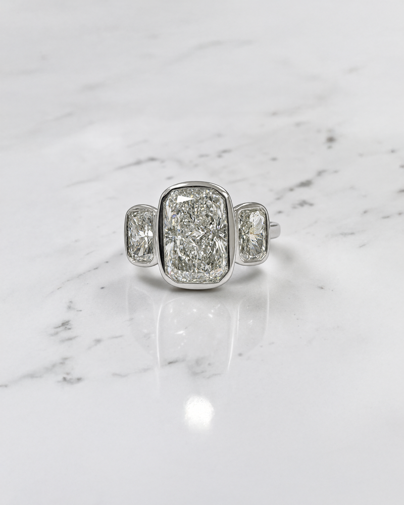 3ct elongated cushion cut lab grown diamond trilogy engagement ring with two 1ct side stones, bezel set rub over setting in polished white metal, handcrafted in London