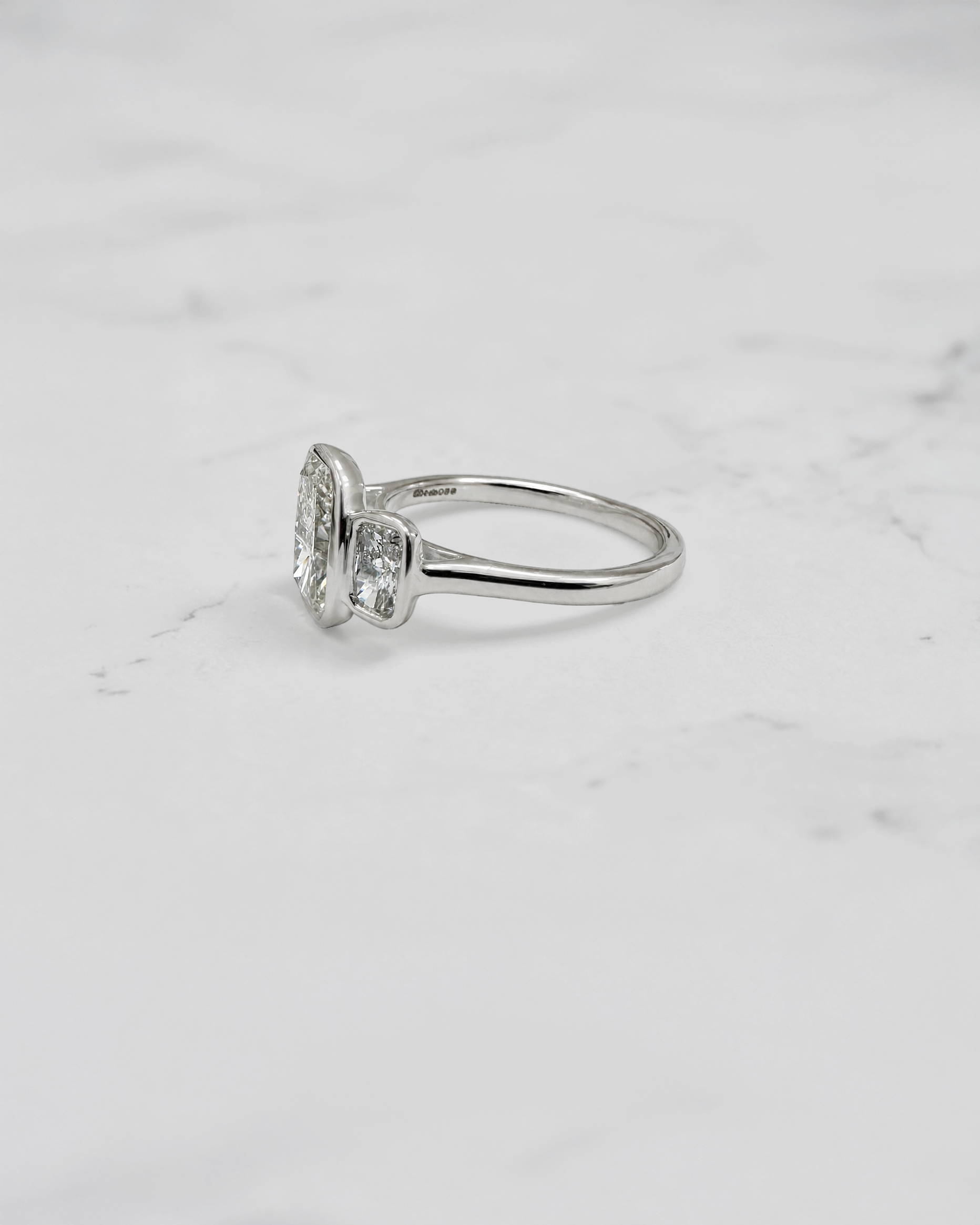 3ct elongated cushion cut lab grown diamond trilogy engagement ring with two 1ct side stones, bezel set rub over setting in polished white metal, handcrafted in London