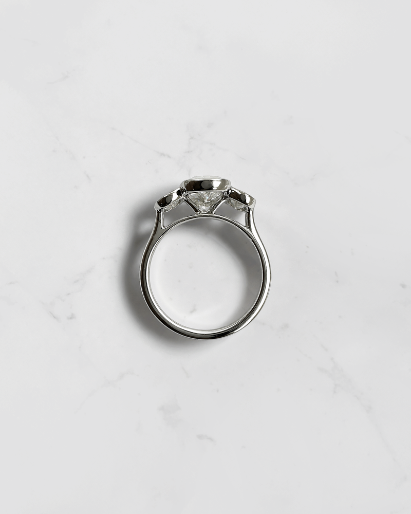 3ct elongated cushion cut lab grown diamond trilogy engagement ring with two 1ct side stones, bezel set rub over setting in polished white metal, handcrafted in London