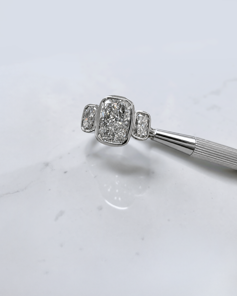 3ct elongated cushion cut lab grown diamond trilogy engagement ring with two 1ct side stones, bezel set rub over setting in polished white metal, handcrafted in London