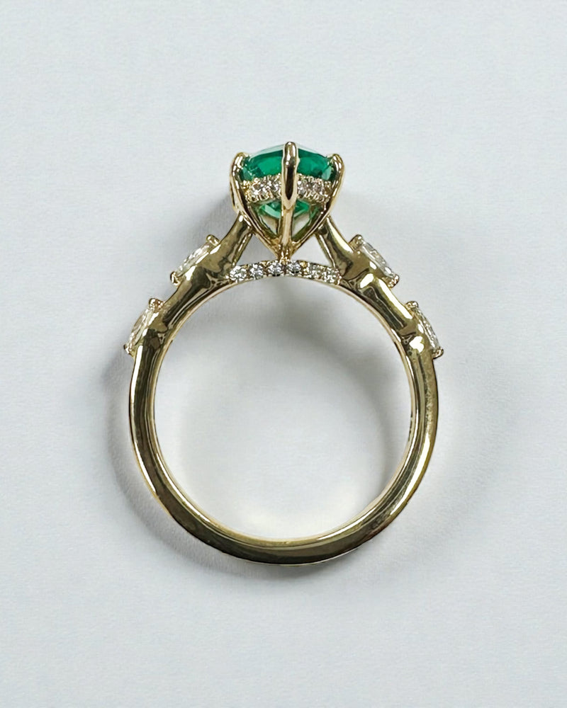 Green emerald marquise engagement ring worn on a finger.