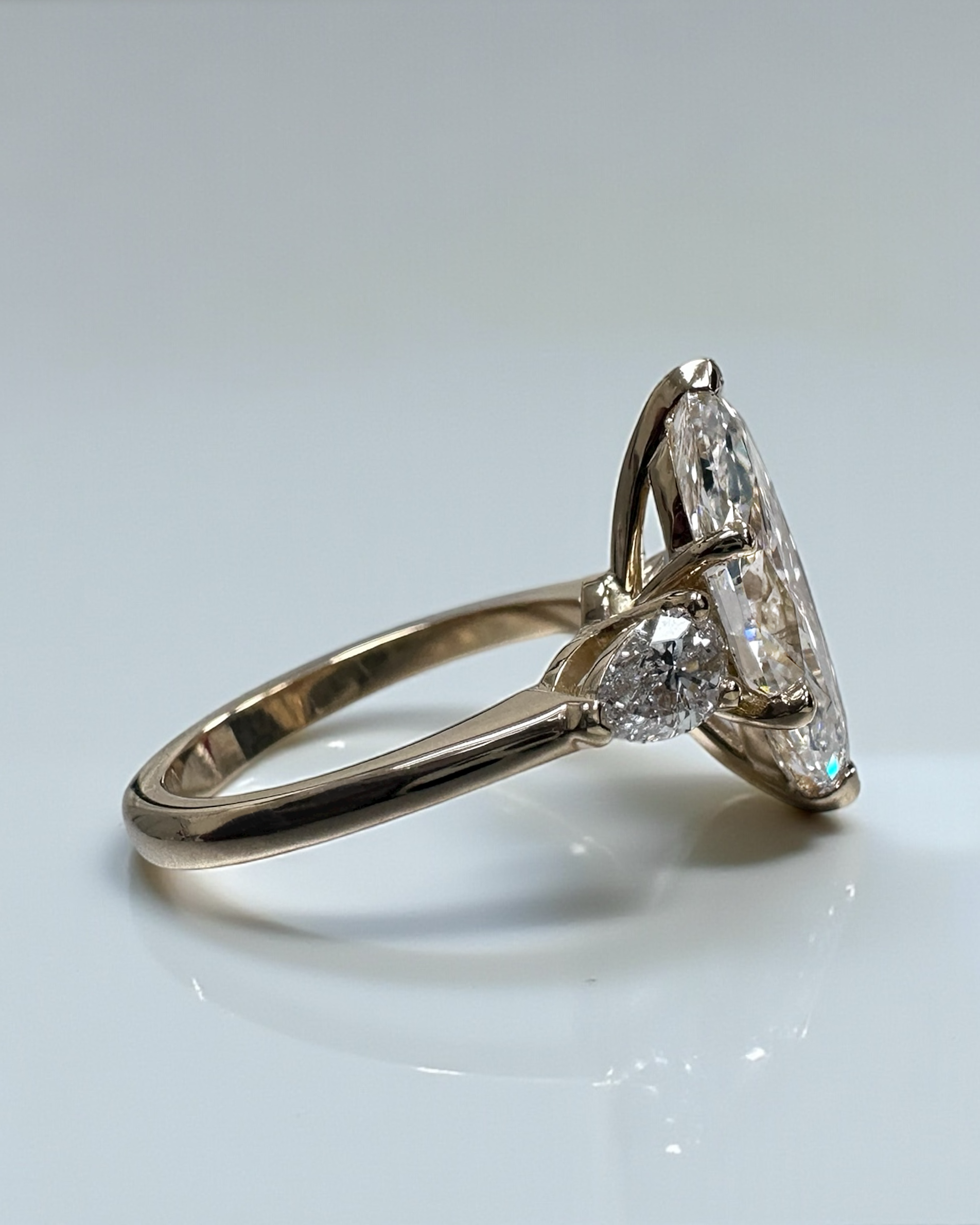 Side view of 3ct marquise cut diamond trilogy ring with pear cut side stones in 18kt yellow gold, showcasing elegant tapered setting and exceptional craftsmanship