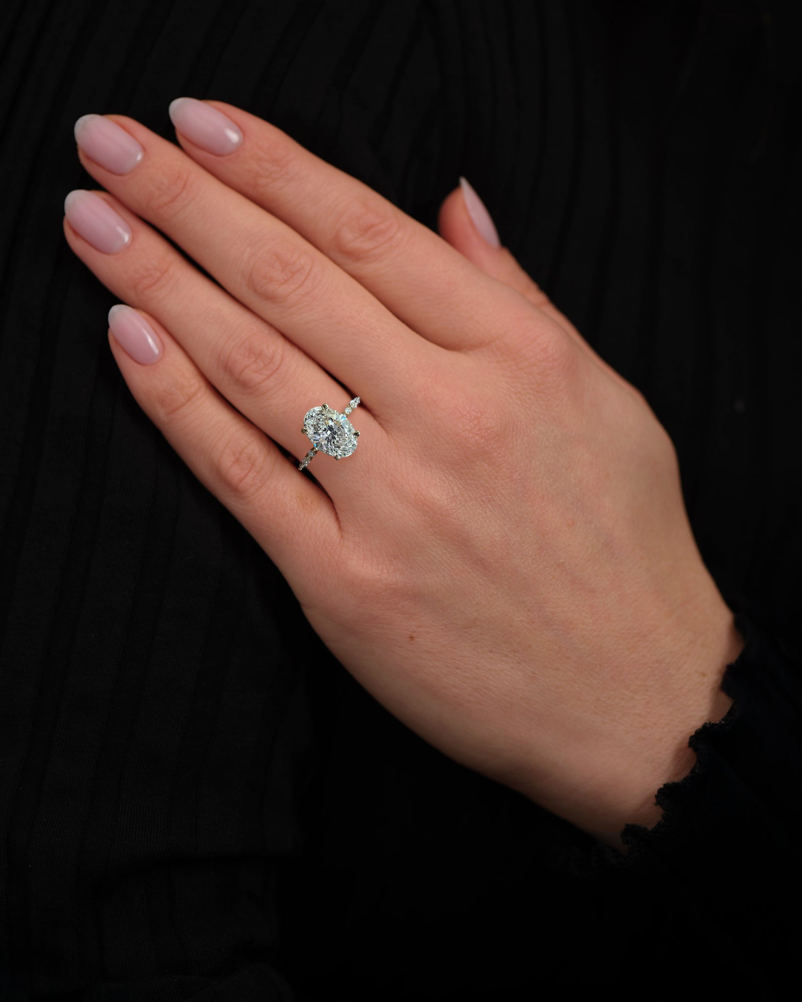 Oval 3ct lab grown diamond engagement ring on hand featuring marquise and round diamond band and delicate hidden halo 18kt yellow gold