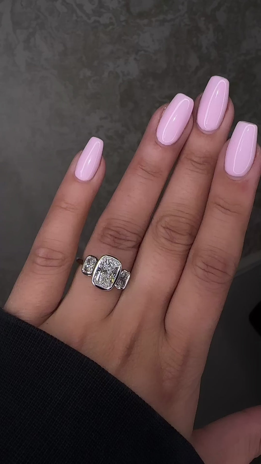 3ct elongated cushion cut lab grown diamond trilogy engagement ring on hand with two 1ct side stones, bezel set rub over setting in polished white metal, 