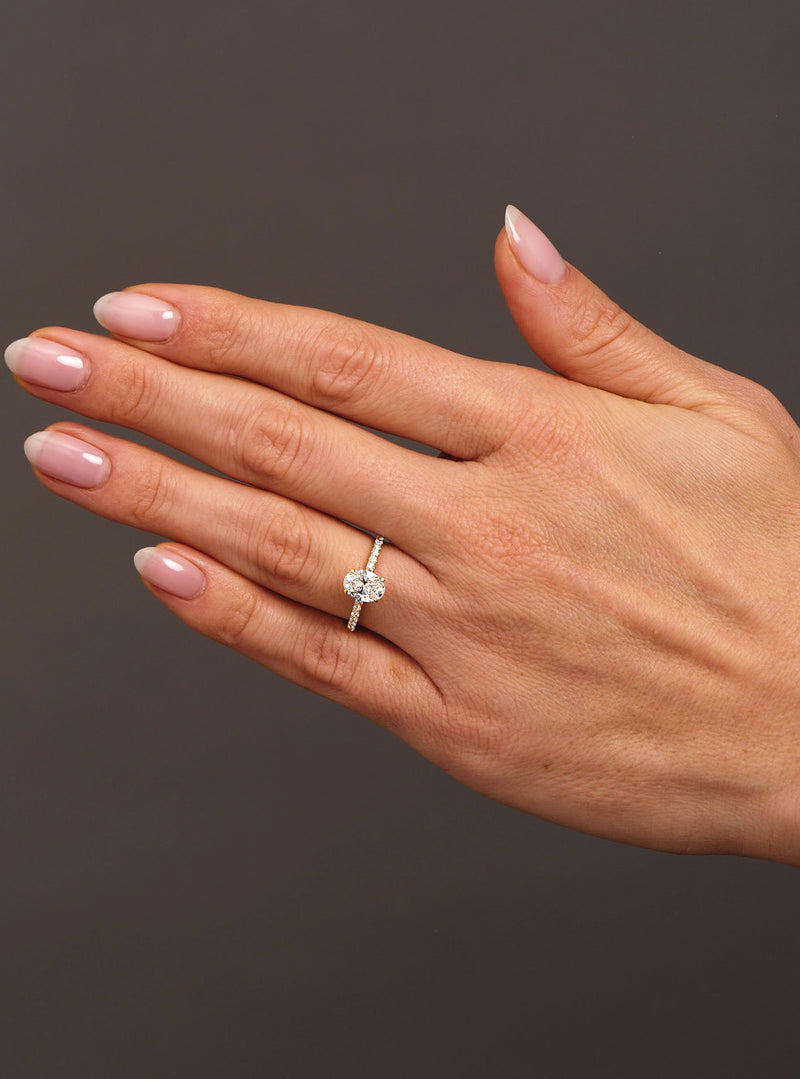 1ct oval cut lab grown diamond hidden halo engagement ring on hand with diamond shoulders by Layla Diamonds